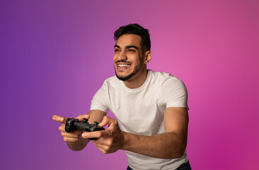 Poster - Happy young Arab guy with joystick playing video game in neon light. Millennial middle Eastern gamer with controller participating in online gaming championship. Modern hobbies concept