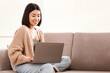 © Prostock-studio - Technology. Millennial Asian Lady Working Remotely On Laptop At Home, Enjoying Freelance Job, Young Woman Sitting On The Couch With Computer, Typing On Keyboard, Watching Video Or Learning