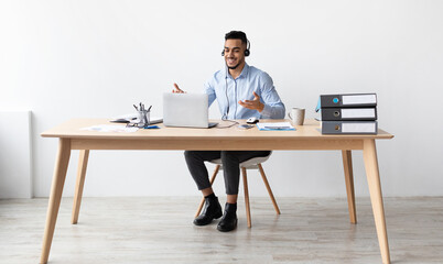 Poster - Video Conference. Portrait of excited Middle Eastern business manager having web call using laptop sitting at desk at workplace in home office, talking and gesturing at pc webcam, wearing headset