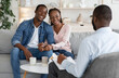 © Prostock-studio - Effective Marital Therapy. Happy african couple sitting on couch at counselor's office, holding hands and smiling, rear view of therapist, free space