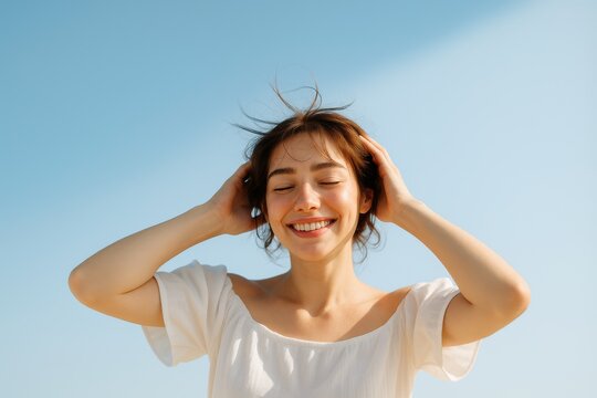 青空の下で目を閉じ幸せそうに微笑む若い女性 | 自然な表情と風になびく髪が開放感を表現 - 健康、幸福、ウェルビーイング、ライフスタイル関連広告やウェブサイト向け