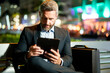 © Volodymyr - Outdoor business. Businessman working on tablet outdoors. Businessman with tablet outdoor. Businessman with a tablet on night street. Businessman using tablet, sit on bench. Night business online.