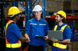© Ekkasit A Siam - Team of warehouse workers in safety equipment shake hands after finishing meeting. Logistic staff with laptop and clipboard stand near storage shelves packed with boxes.