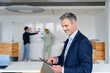 © Westend61 - Businessman using a tablet in a modern office with colleagues in the background