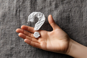 Poster - Child's hand holds fabric question mark on gray textile background, symbolizing uncertainty, inquiry, or seeking answers