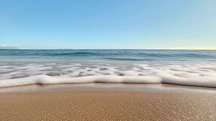 Poster - Soft waves gently rolling onto a sandy beach on a bright sunny day, creating a serene and peaceful atmosphere with clear blue sky and tranquil ocean waters