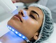 © TransPicHub - A woman receives a facial treatment with a blue LED light device at a skincare clinic.