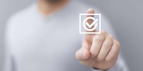 Fototapete - Man in gray sweater is touching a digital checkmark icon on a transparent screen, symbolizing approval and confirmation in a modern technological environment