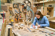 © Robert Kneschke - Young woman learning woodworking skills in a busy workshop