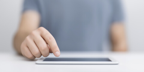 Poster - Close-up of a hand interacting with a tablet device on a clean surface, showcasing modern technology and user engagement in a minimalist workspace environment