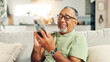 © peopleimages.com - Home, laughing and senior man with smartphone, relax and texting with tech in living room, smile and online. Communication, retirement and elderly person with mobile for chat, message or social media
