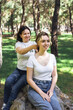 © Alina - Smiling mother tying teenage daughters hair while sitting outdoors