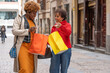 © Ceballos - Two smiling women showing shopping bags on a city street