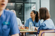 © Maskot - Happy young female nurse sitting with colleagues at table for breakfast in hospital cafeteria