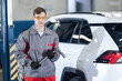 © Parilov - Caucasian male auto mechanic holding tool in garage near white suv