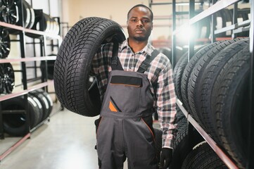 Poster - Car tire service concept. Portrait African american man mechanic holding new tyre on background store