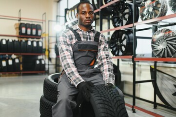 Poster - Car tire service concept. Portrait African american man mechanic holding new tyre on background store