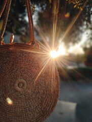 Aufkleber - Sun Lens Flare Shines Through Round Straw Purse During Sunset at a Calm Outdoor Location Generative AI