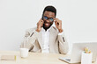 © SHOTPRIME STUDIO - Smiling man with dark skin, curly black hair, wearing glasses and beige blazer, working at desk with laptop and cup on bright white background, business casual style, professional, relaxed, modern