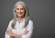 © Vooglo.com - Smiling mature woman with gray hair and arms crossed posing in a white shirt against a gray background