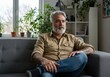 © Vooglo.com - Thoughtful mature man with gray hair and beard relaxing on a gray couch in a bright living room