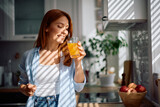 Happy woman drinking orange juice in kitchen.