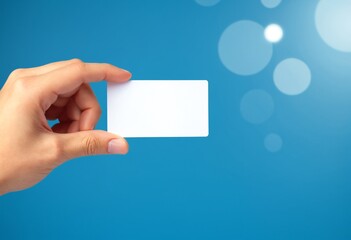 Fototapete - A hand holds a blank white card against a blue background with soft circular light effects