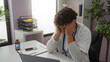 © Krakenimages.com - Young hispanic male doctor in hospital office feeling stressed at desk with stethoscope and files, highlighting workplace challenges and professional pressures.