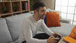 © Krakenimages.com - Young man playing video games indoors with a game controller, smiling and relaxed, sitting in a modern living room with stylish decor, captured in a cozy home atmosphere.