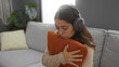 © Krakenimages.com - Woman relaxing indoors listening music with headphones hugging cushion in cozy apartment setting creating peaceful atmosphere.