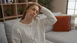 © Krakenimages.com - Woman stretching neck indoors on sofa in cozy living room, displaying relaxation and comfort amidst neutral tones and modern decor.