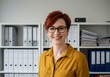 © Laki - Portrait of smiling woman with red hair and glasses in front of white shelves with folders and papers