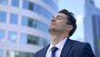 © AI_ALICE - 白人のビジネスマン男性が目を閉じておフィルビルの前に立つ様子。AIで生成
