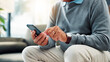 © FrameFlex/peopleimages.com - Senior man, hands and typing with phone on sofa for game, word search or social media app at home. Closeup, male person or elderly user browsing with mobile smartphone for connection or network
