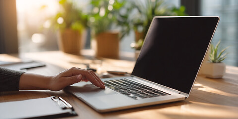 Poster - Laptop on wooden table, hand on touchpad, sunlit workspace, showcasing productivity and modern technology