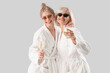 © Pixel-Shot - Happy young woman and her mother in bathrobes with glasses of champagne on grey background
