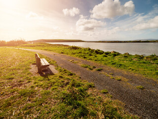 Wall Mural - one wooden old bench by a walking path with stunning view on open space with lake and amazing blue c