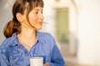© rh2010 - Close-up of a serene woman in blue linen holding a ceramic cup, bathed in warm morning light beside a traditional trullo home in southern Italy