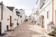 © rh2010 - A peaceful narrow street in Alberobello, Italy, lined with traditional trulli houses featuring conical stone roofs, whitewashed walls, and potted greenery. A timeless southern charm