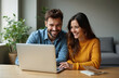 © miss irine - Happy couple looking laptop screen. Smiling man and woman using computer, sharing online content, enjoying digital entertainment together at home, relaxed. Modern relationships, digital era.
