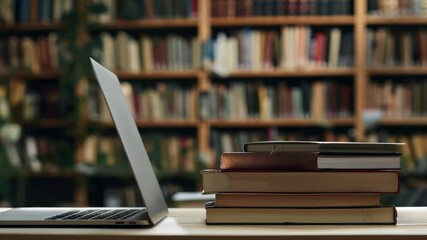 Aufkleber - This image shows a laptop and stacked books on a wooden table with a full bookshelf in the background, suggesting a setting for study, research, and learning in school or university.