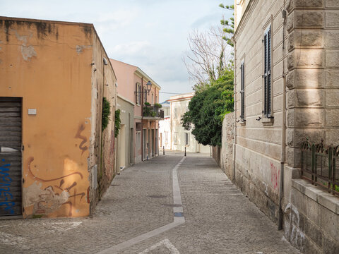 Horizontal Wide-Angle View of a Cobblestone Street with Orange Facade and Tree in Olbia Old Town, Sardinia, Italy