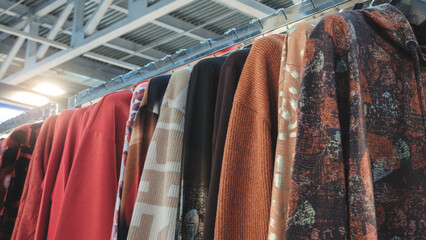 Poster - A row of clothes hanging on a rack, including a red shirt with a black stripe and a brown shirt with a gold leaf design