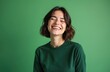 © miss irine - Joyful woman with closed eyes against green background. Attractive female brunette with big smile, white teeth. Portrait of happy girl shows positive emotions. Model wearing dark green clothes in