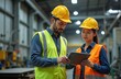 © miss irine - Senior engineer trains new employees in metal sheet factory. Workers wear safety vests and hard hats. Staff uses tablet, inspects production process. Modern industrial facility with machinery.