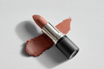 Poster - A luxurious lipstick in a nude shade with a silver tube and black bottom, accompanied by swatches on a clean, light surface highlighting the color and texture.