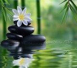 Stack of smooth black spa stones with a white plumeria flower on top, surrounded by bamboo leaves and reflected in calm green water, evoking tranquility and relaxation