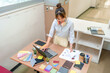 © snowing12 - Asian Woman Interior Designer Working on Laptop with Color Swatches Fabric Samples and Design Sketches Creative Workspace for Design Projects