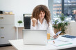 © Phushutter - Confident Russian consultant sits at modern desk, analyzing market data on laptop. reports and charts, she embodies precision, leadership, and strategic mindset of corporate consulting.