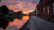 © AN STOCK - Sunset reflections over canal path lined with historical buildings